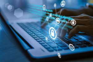 persona escribiendo en un computador, con símbolos de ciberseguridad flotando
